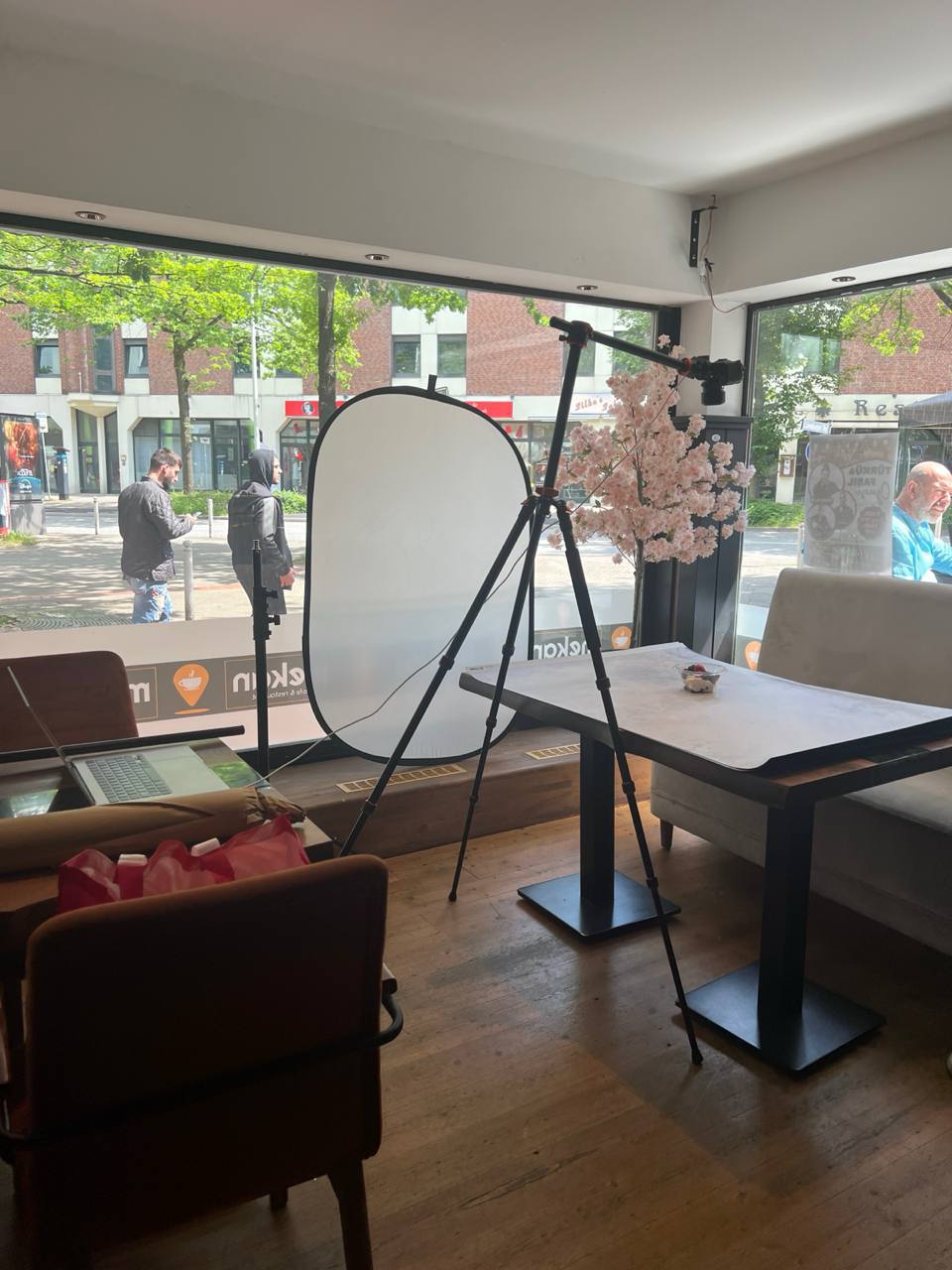 My shooting setup inside a restaurant: tripod, reflector, camera on one dish, laptop off to the side.